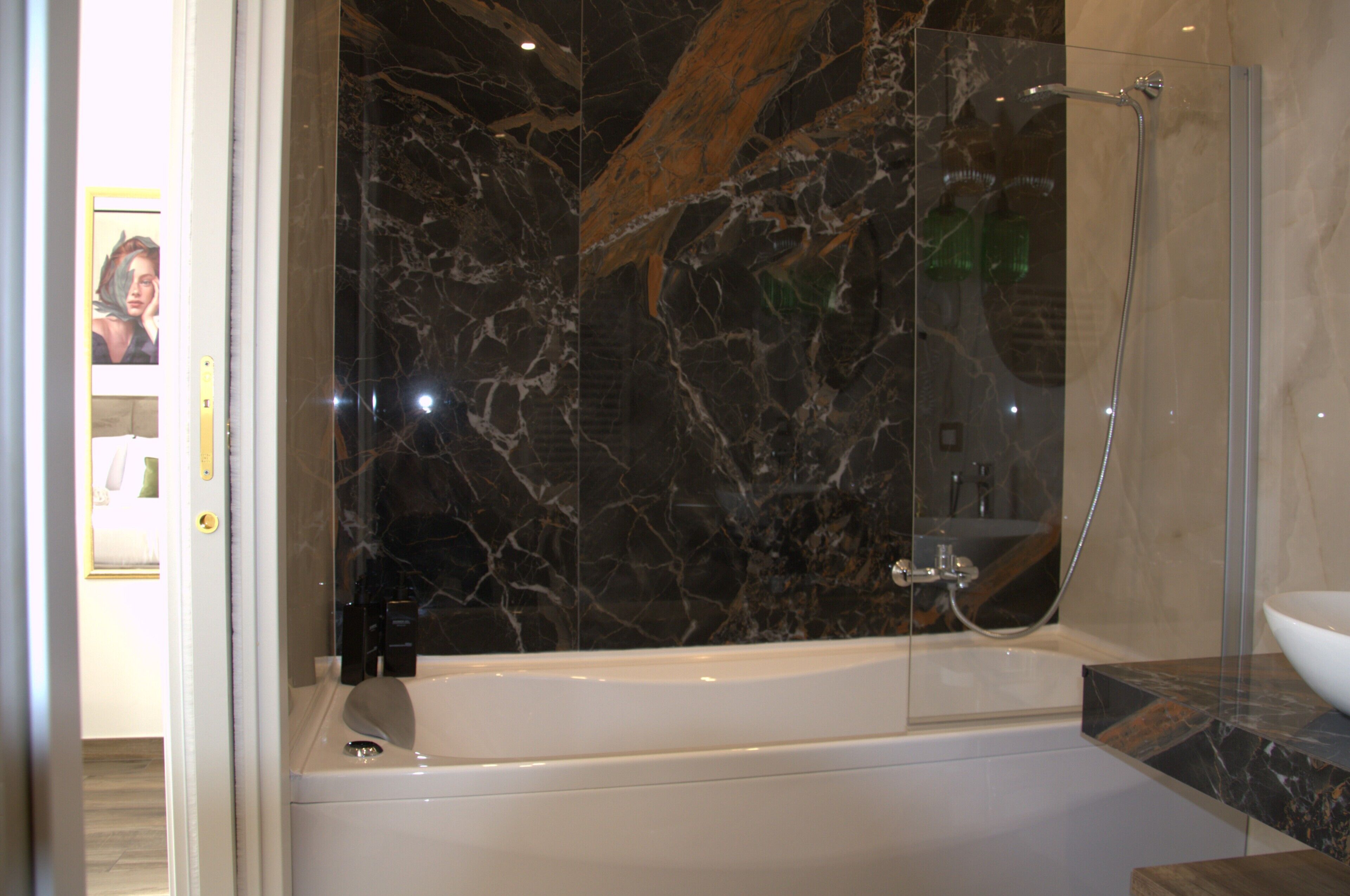 A modern bathroom with a marble wall, a bathtub, and a glass-enclosed shower area.
