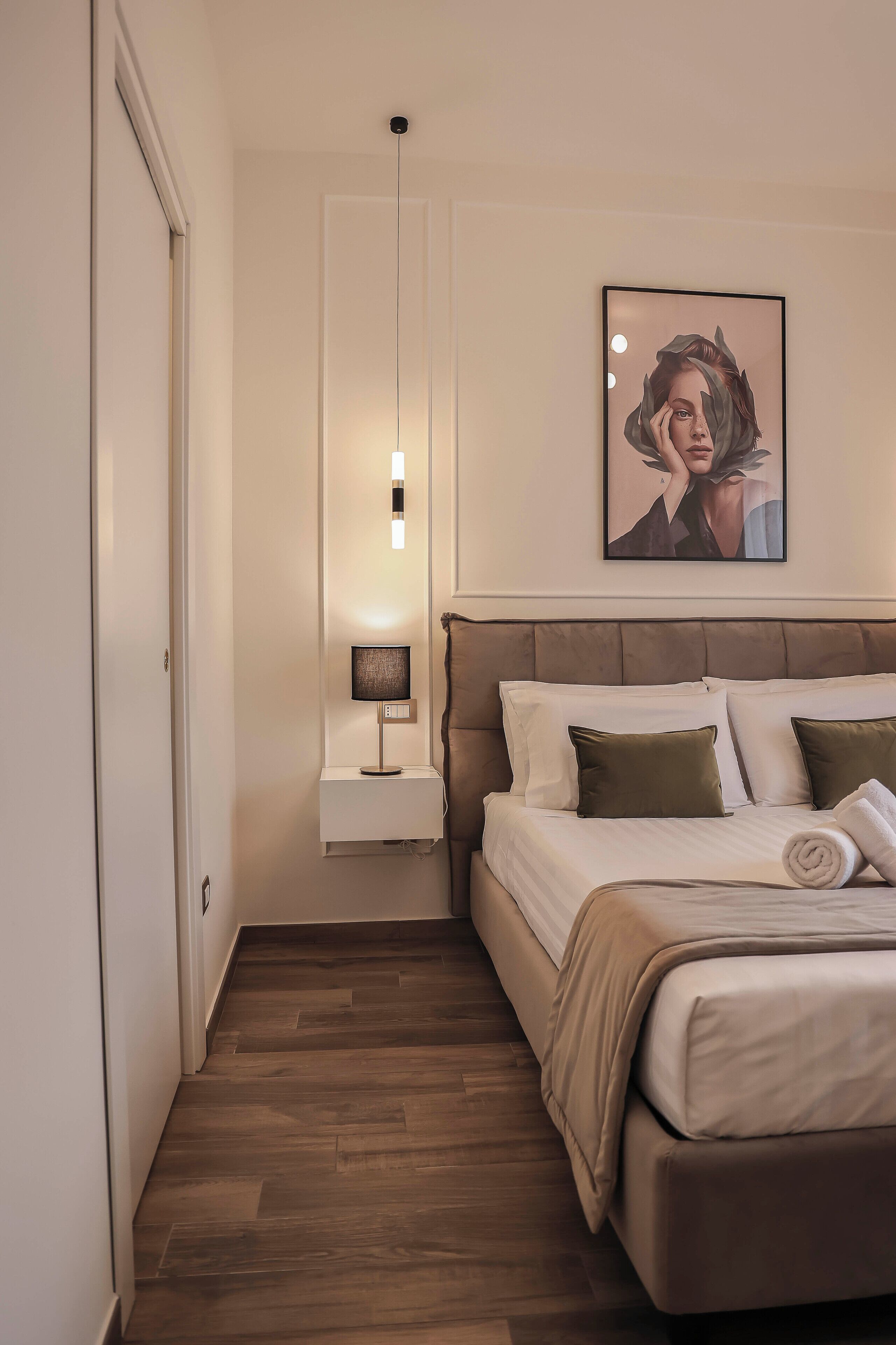 A bedroom with a bed, a nightstand, a wall-mounted lamp, and a framed picture.