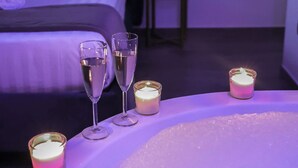 Et værelse med seng, et natbord og et badekar med stearinlys og glas med vand.