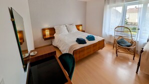 A bedroom with a wooden bed, a chair, a desk, and a large window with curtains.