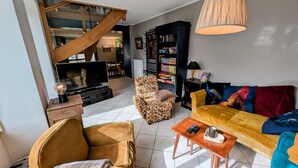 A living room with a sofa, armchair, and a coffee table. There is a bookshelf and a television in the background.
