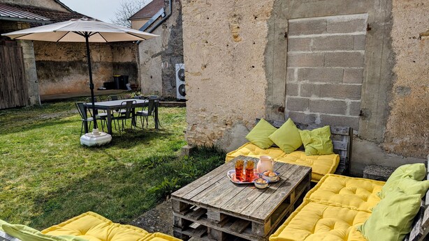 An outdoor seating area with a wooden table, yellow cushions, and a table set with glasses and a pitcher.