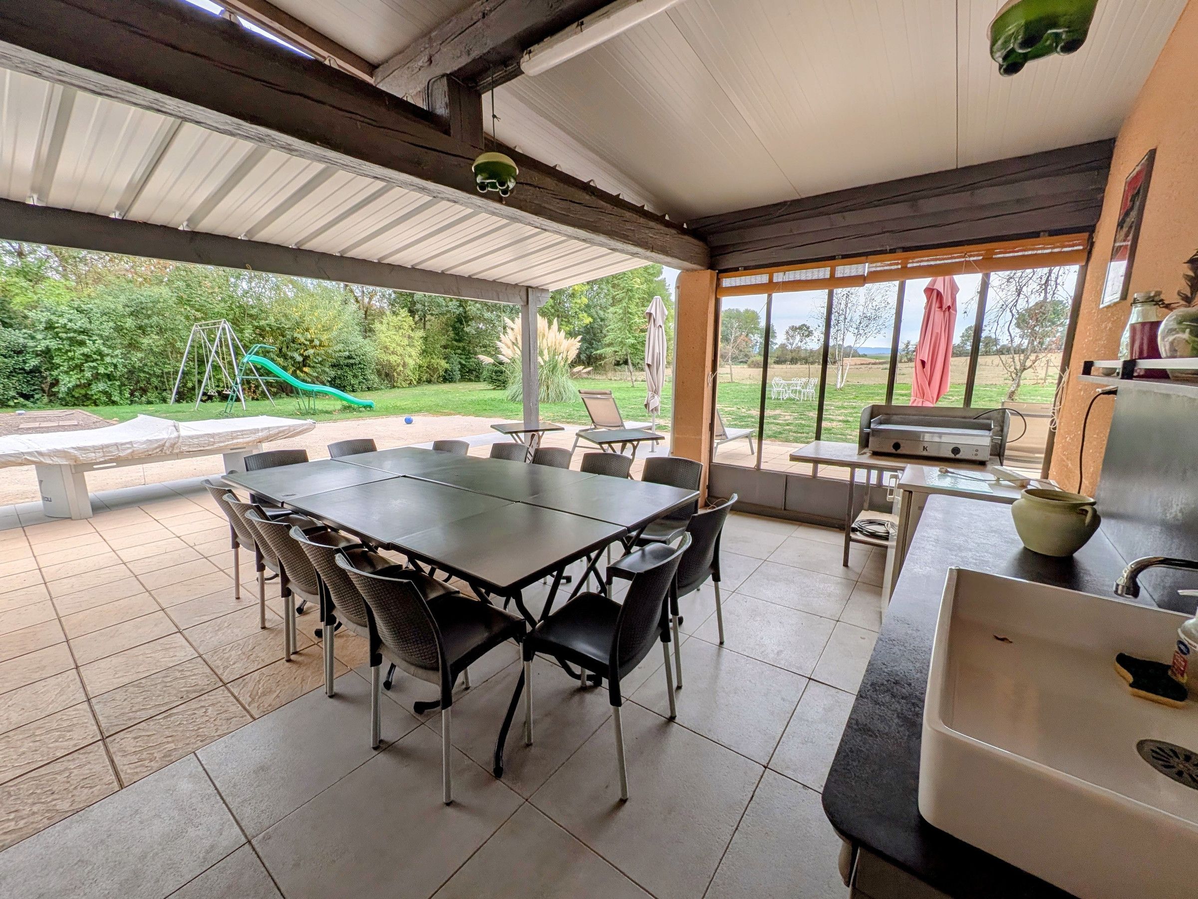 An outdoor patio with a table and chairs, a grill, and a view of a playground.