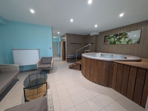A modern living room with a glass-top coffee table, a sofa, a chair, a wooden cabinet, and a hot tub. - Charming cottage in Ognon valley with spa (Bay)