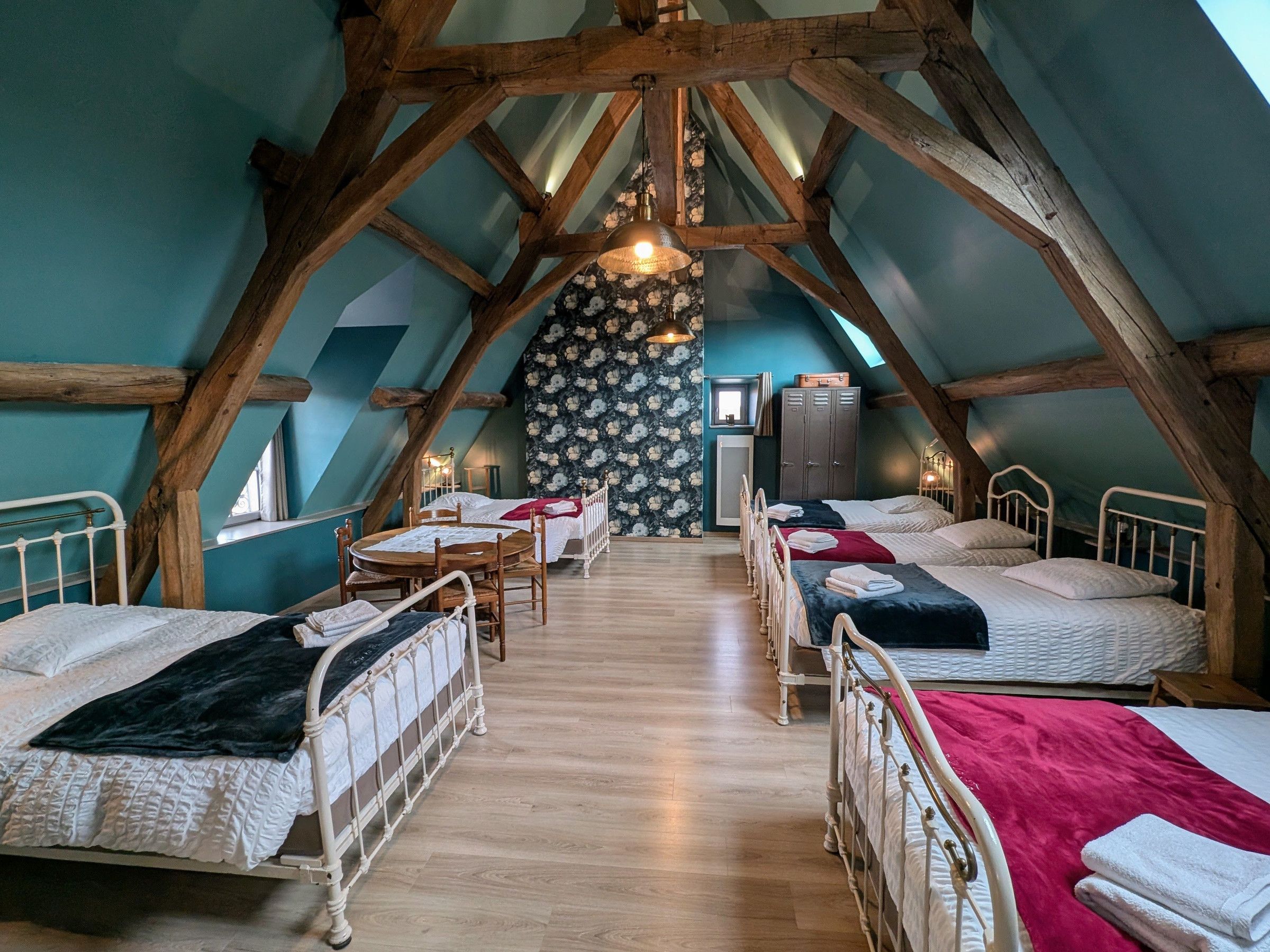 A cozy attic bedroom with wooden beams, a floral wallpaper, and a small table with chairs.