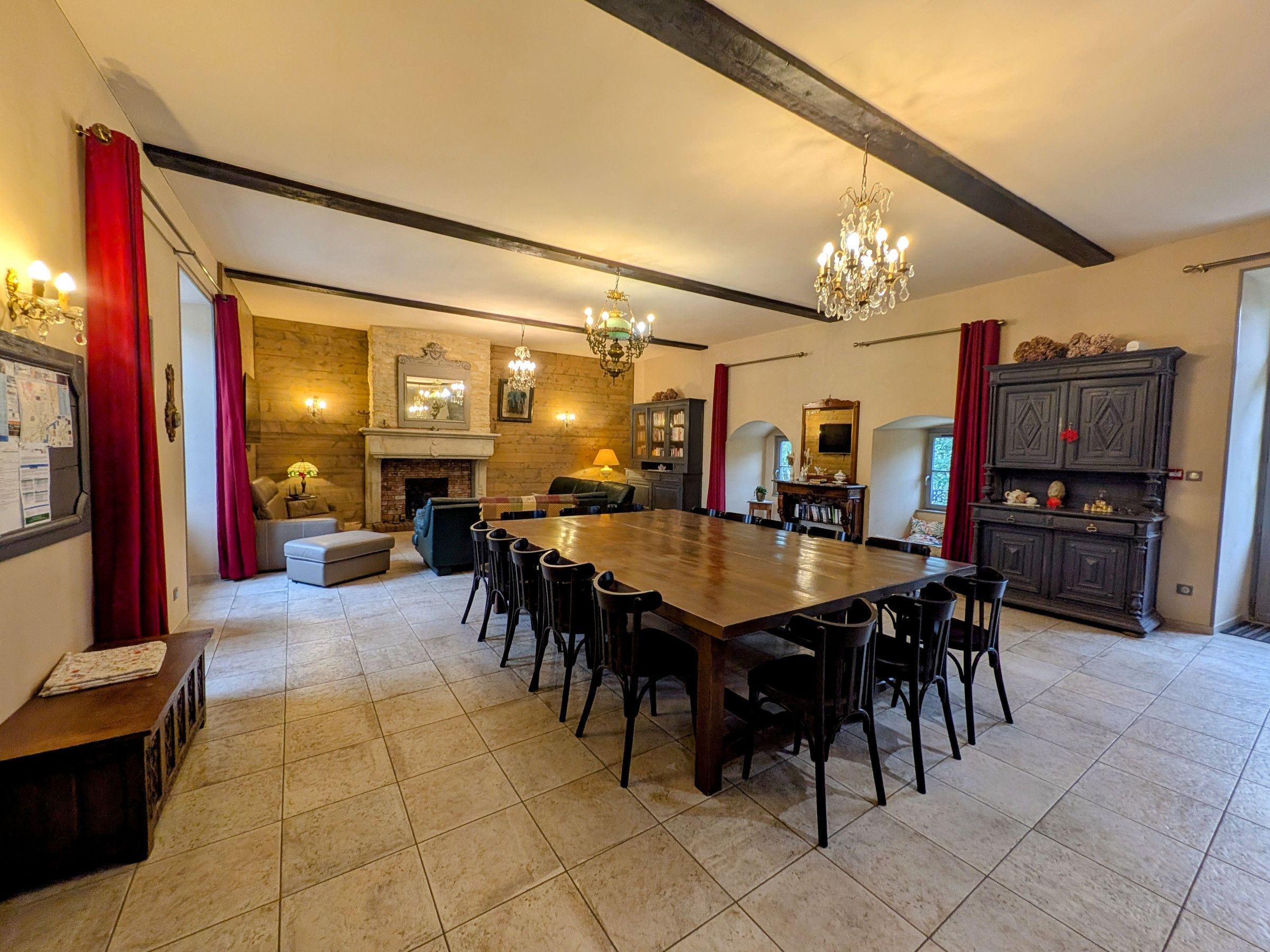 A spacious dining area with a large wooden table and chairs, a fireplace, and a chandelier.