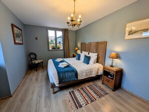 Un dormitorio con cama, una silla, mesita de noche, lámpara, candelabro, ventana y alfombra.