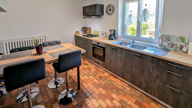 Une cuisine moderne avec un coin repas, comprenant une fenêtre avec des rideaux, une cuisinière encastrée et un évier.