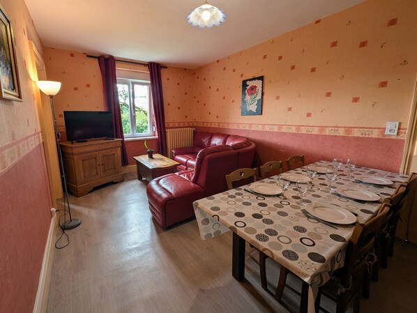 Ein Essbereich mit einem Tisch für vier Personen, einem roten Ledersofa, einem Fernseher und einem Fenster mit Vorhängen.