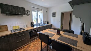 Une cuisine moderne dotée d’un îlot central, de meubles de couleur sombre et d’un coin repas agrémenté de sets de table à motifs.