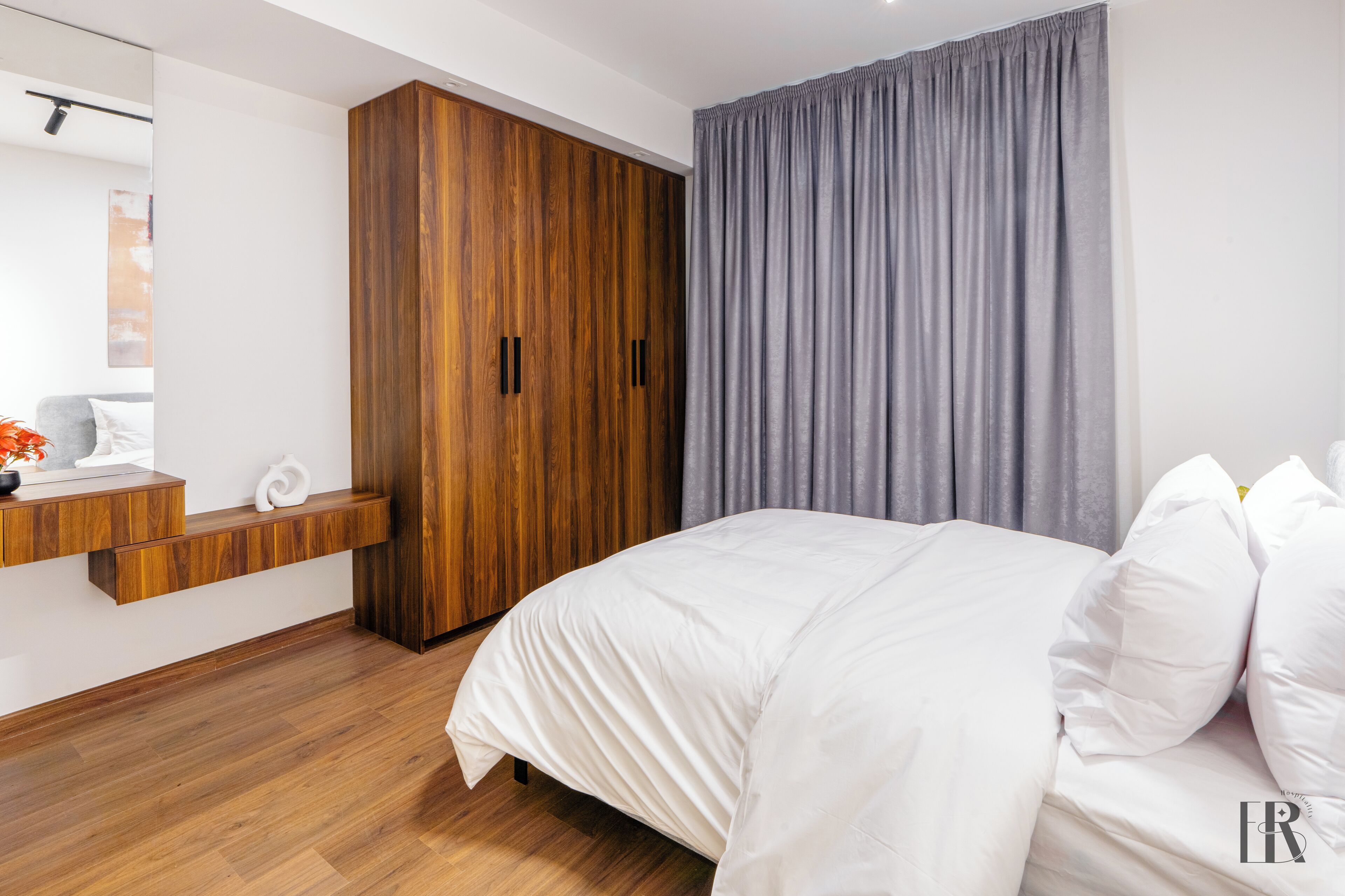 A modern bedroom with a wooden wardrobe, a grey curtain, and a white bed.