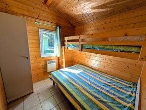 Una habitación pequeña y acogedora con una cama litera, una ventana con cortinas, un radiador y una puerta.