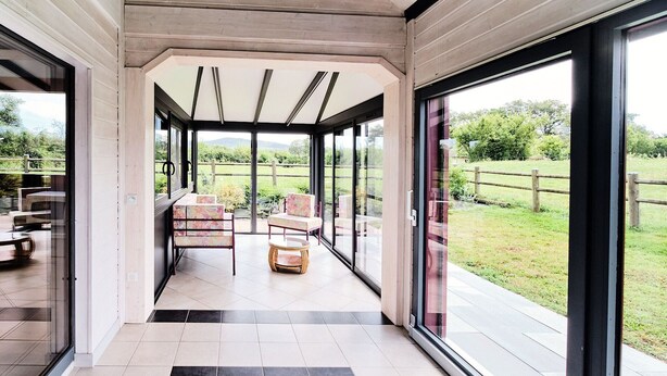 Un interior moderno con puertas de cristal grandes que dan a un jardín. Hay dos sillas y una mesita en el centro.