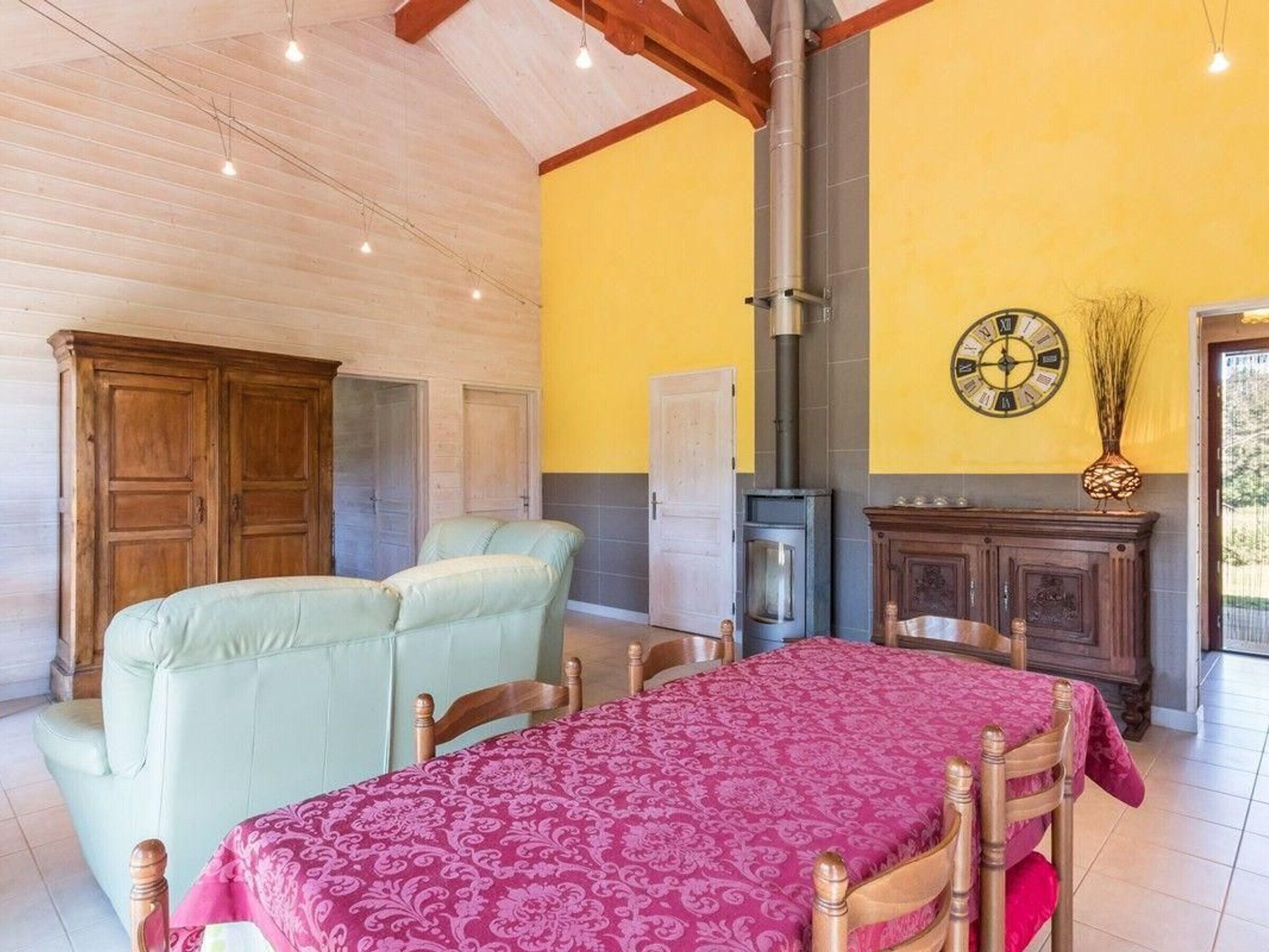A room with a bed, a wooden wardrobe, a table with chairs, a fireplace, and a clock on the wall.