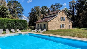 Ein Steinhaus mit Swimmingpool, umgeben von Grün und Liegestühlen.