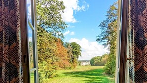 Eine offene Tür, die zu einer grünen Fläche mit Bäumen und einem entfernten Gebäude führt.