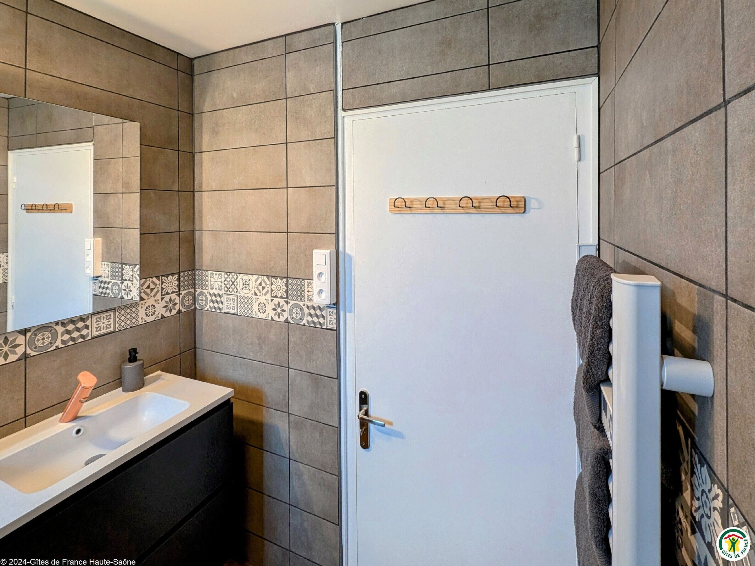 A bathroom with a white door, a sink with a soap dispenser, and a towel rack.