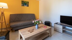 Un salon moderne avec un canapé gris, une table basse en bois sur laquelle est posé un vase de fleurs, une lampe et un téléviseur à écran plat sur un meuble en bois.