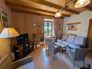 Una habitación con paneles de madera, un sofá, dos sillones de mimbre, un televisor, una estantería y una ventana con cortinas.