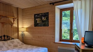 Une pièce en bois avec un lit, un bureau avec un ordinateur, une fenêtre avec des rideaux et une lampe fixée au mur.