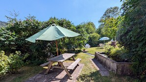 Une table de pique-nique avec un parasol vert, entourée d’une végétation luxuriante et d’un petit étang.