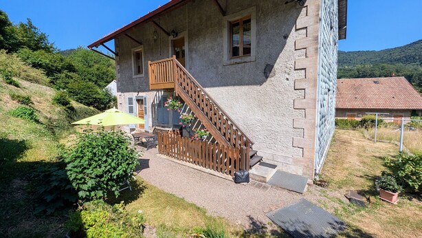 Un bâtiment en pierre doté d’un escalier en bois, d’un petit balcon et d’un jardin agrémenté de plantes en pot.