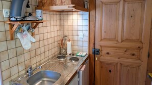 A kitchen with a stainless steel sink, wooden cabinets, and a coffee maker on a shelf.