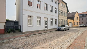 Eine Kopfsteinpflasterstraße gesäumt von mehrstöckigen Gebäuden, ein geparktes Auto und ein schmaler Bürgersteig.
