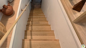 Un escalier en bois, doté d’une rampe, mène à un palier où se trouvent une plante et un pot en terre cuite.