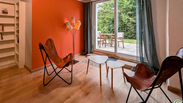 Un salon moderne doté d’une grande porte-fenêtre coulissante donnant sur une terrasse, d’une bibliothèque et de deux fauteuils en cuir.