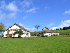 A white house with a red roof and a smaller adjacent building, surrounded by a green field and trees under a clear blue sky. - Charming Cottage in the Vosges Saônoises (Saint-Bresson)