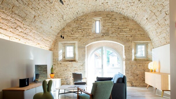 Ein geräumiges Wohnzimmer mit Stein-Gewölbekonstruktion, einem großen Bogenfenster und einem modernen Sofa.