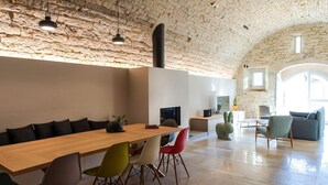 Ein geräumiger Essbereich mit einem langen Holztisch und bunten Stühlen, einer Steinwand und einer modernen Küche im Hintergrund.