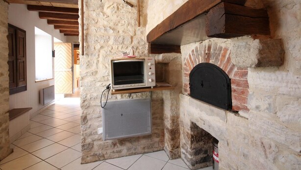 Una cocina rústica con pared de piedra, horno de ladrillo y una pequeña encimera con microondas.