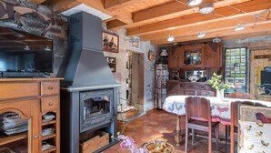 A rustic interior with a wood-burning stove, wooden cabinets, a television, and a dining area with a table and chairs. - Family cottage for 8, historic charm & modern comfort (Fresse)