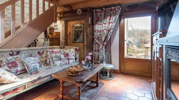 A cozy room with a wooden staircase, a sofa with patterned cushions, a wooden table, and a view through a window. - Family cottage for 8, historic charm & modern comfort (Fresse)