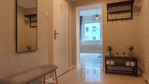 A hallway with a bench, a mirror, a console table with shoes, and a view of the outside. - Castora Homes - City Apartment Kassel near train station (Kassel)