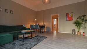 A modern living room with a green sofa, a coffee table, and a dining area with chairs. - Castora Homes - City Apartment Kassel near train station (Kassel)