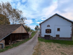 A rural road leading to a white building with a stone foundation and a wooden barn on the left.