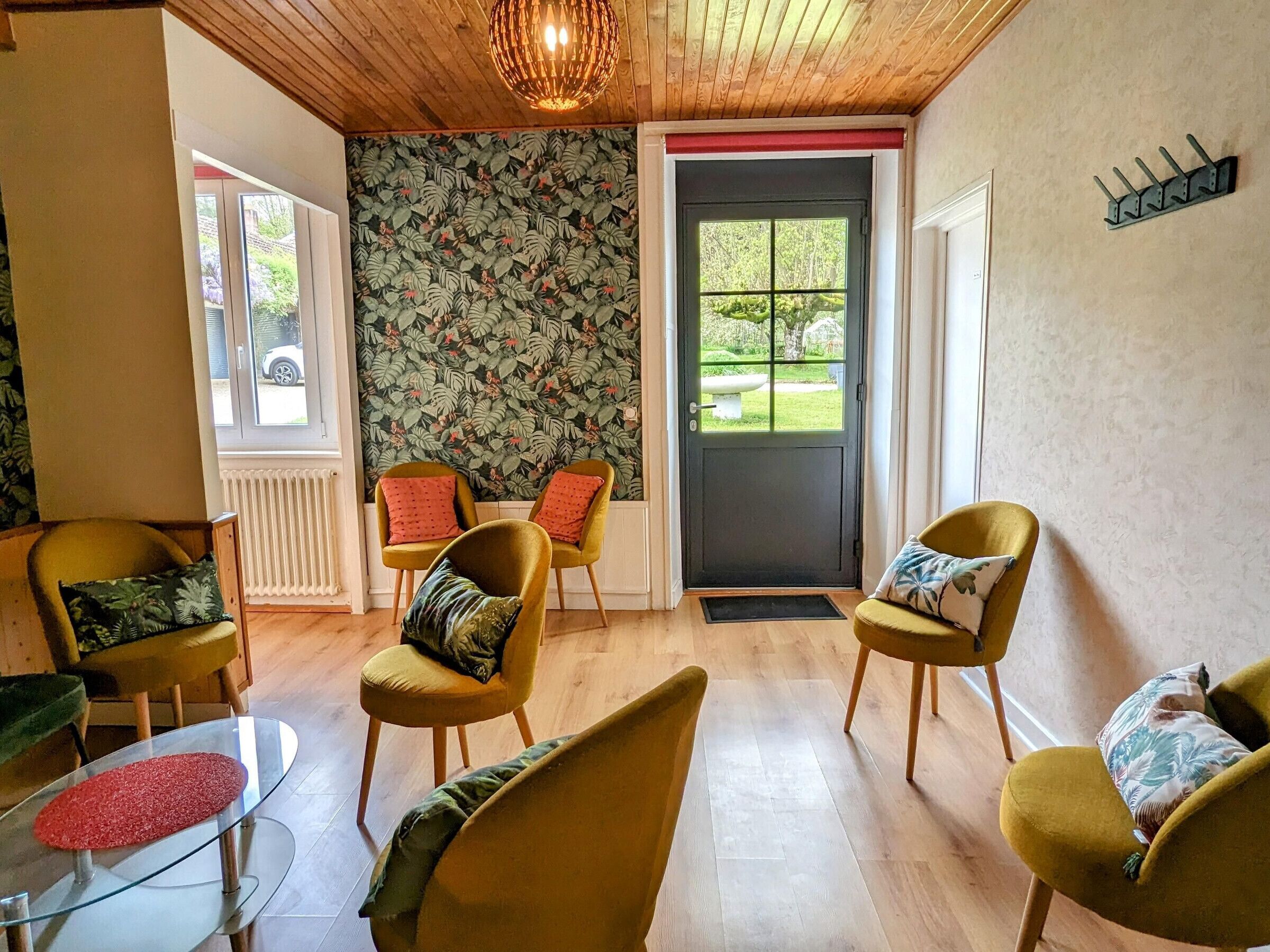 A room with wooden flooring, yellow chairs, a glass table, and a door with a view of greenery outside.