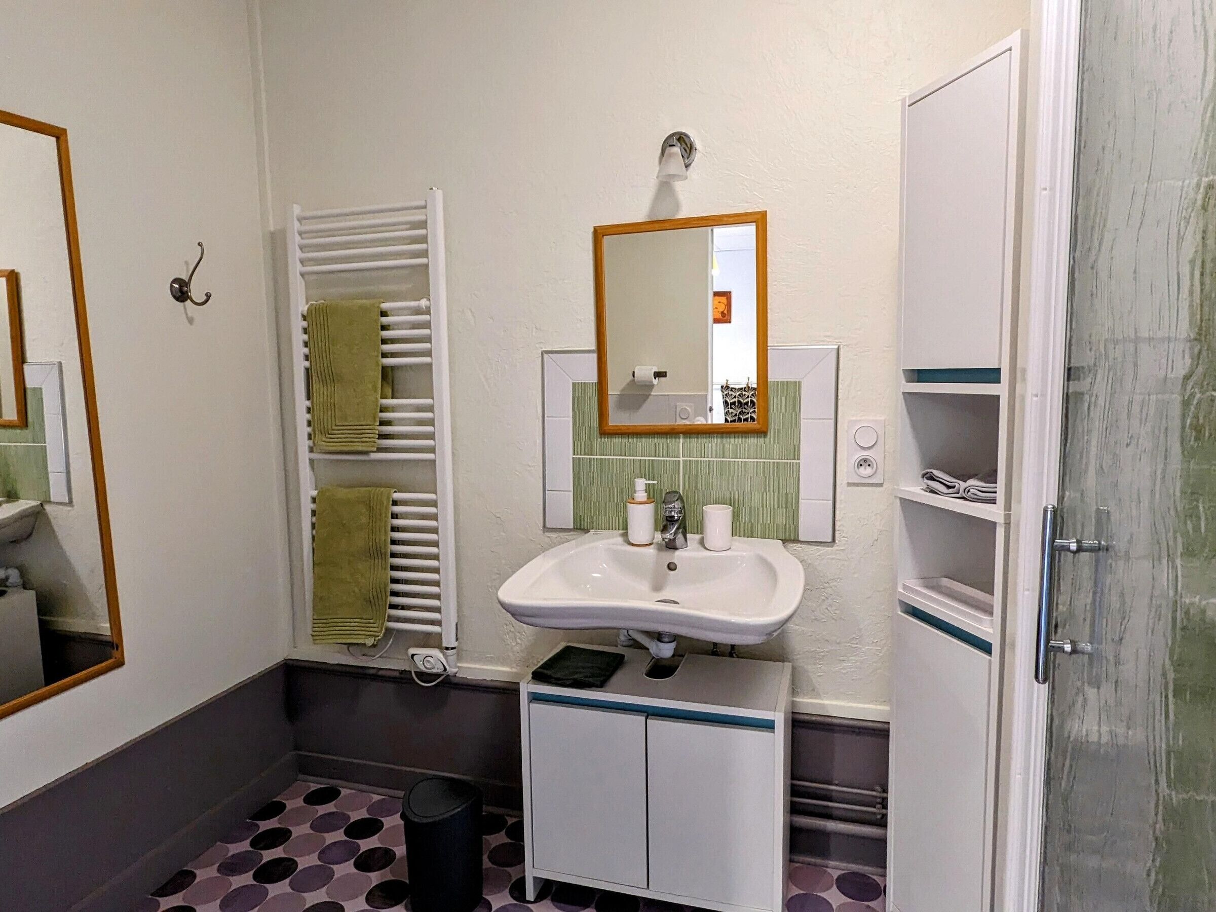 Een badkamer met een wastafel, spiegel, handdoekhouder en een prullenbak.