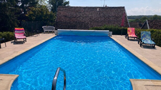 Piscina retangular com escada de metal em primeiro plano, cercada por espreguiçadeiras e um deck revestido de azulejos.