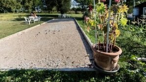 Um jardim com uma quadra de areia alongada e estreita, rodeada por vegetação e plantas em vasos.