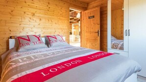 Une chambre à coucher dans une cabane en bois, avec un lit recouvert d’une couverture à rayures rouges et blanches, une tête de lit en bois et une porte donnant sur un placard.