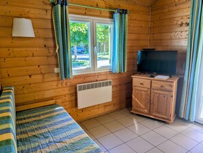 Una habitación con una cama, un televisor sobre un mueble de madera, una ventana con cortinas y un radiador.