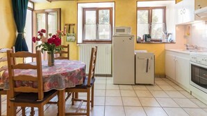 A compact kitchen with a dining area, featuring a refrigerator, microwave, stove, and a small table with chairs. - Cozy single-story cottage in Confracourt, nature and relaxation (Confracourt)