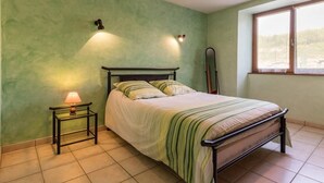 A bedroom with a bed, a nightstand, a lamp, a mirror, and a window. - Cozy single-story cottage in Confracourt, nature and relaxation (Confracourt)