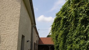 A narrow street with a wooden fence, a building with a red roof, and a green hedge. - Cozy single-story cottage in Confracourt, nature and relaxation (Confracourt)