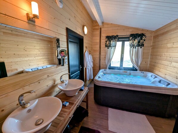 Baño de cabaña de madera con dos lavamanos, una bañera, un espejo y una ventana con cortinas.
