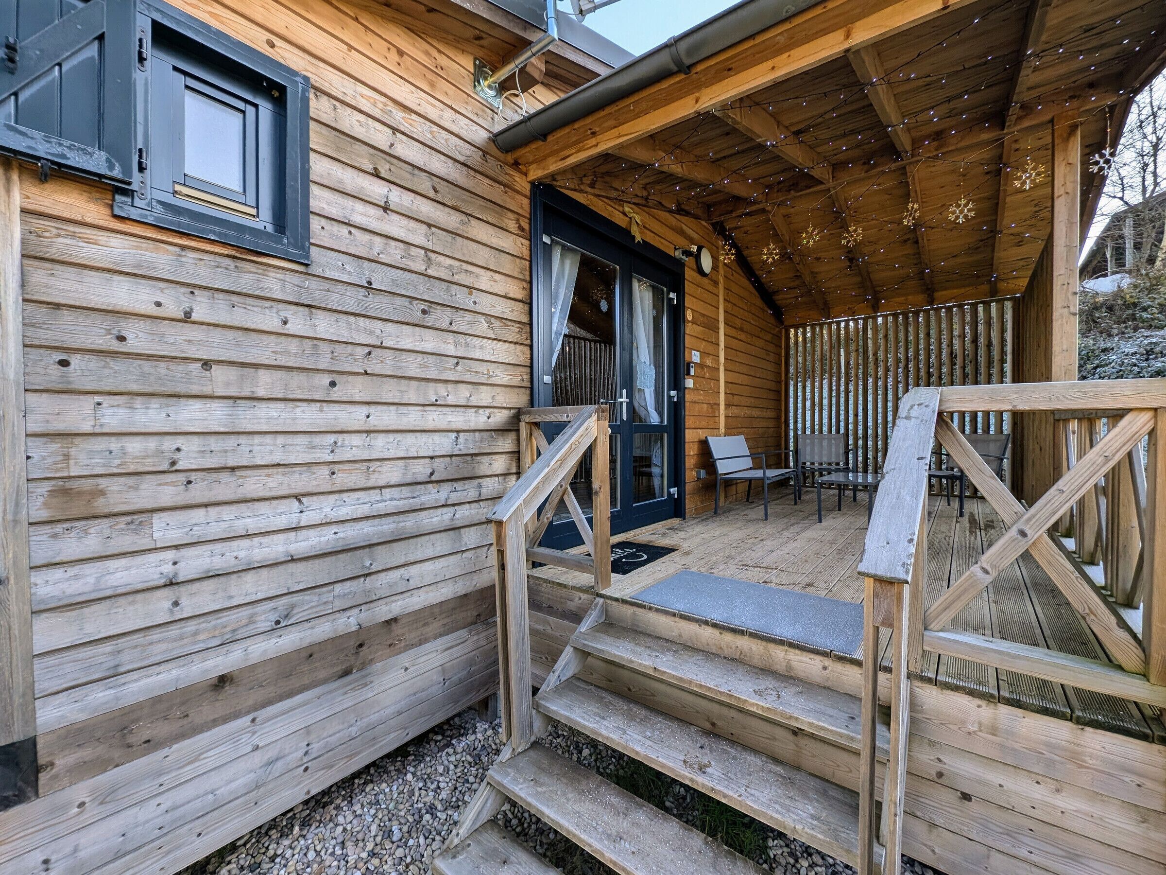 A wooden cabin with a covered porch, steps leading to a door, and outdoor seating.